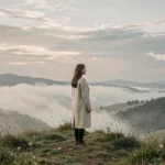 Femme contemplative au sommet d'une colline brumeuse regardant l'horizon, évoquant les signes d'une grande destinée